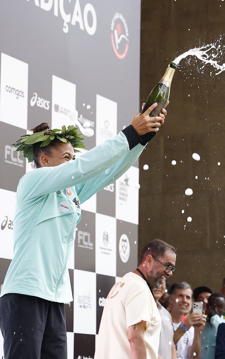 Atleta comemorando no pódio com champagne e coroa de louros